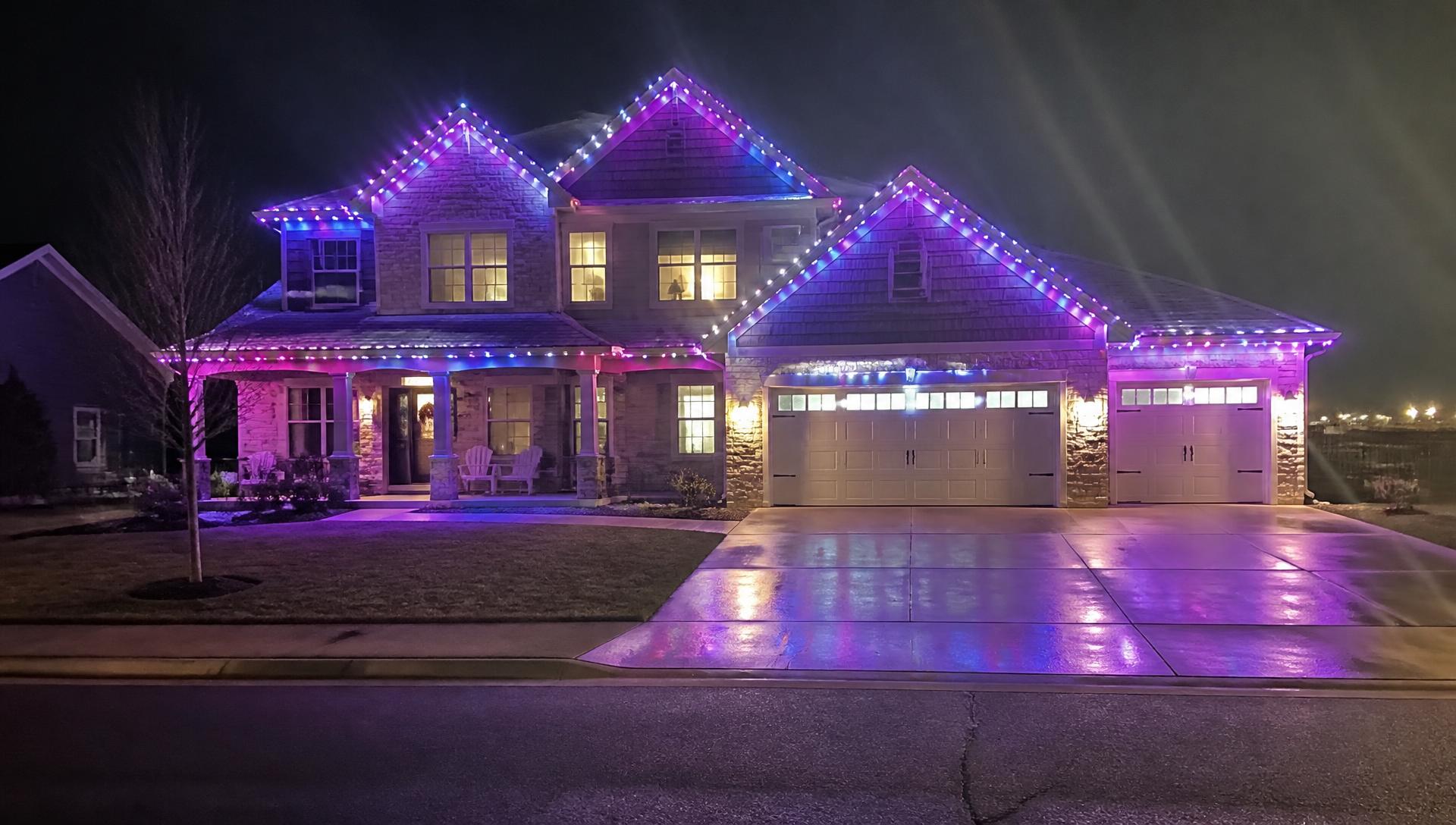 Two-storey home at night lit with permanent RGB LED lights in blue, purple and magenta along every roofline